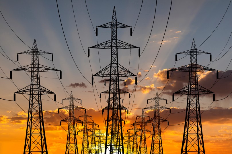 A photo of electric transmission towers and wires with a sunset backdrop.